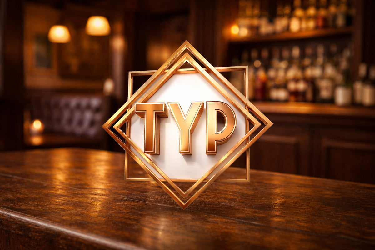 TYP logo in gold frame on wooden bar, bourbon whiskey scotch bottles in background
